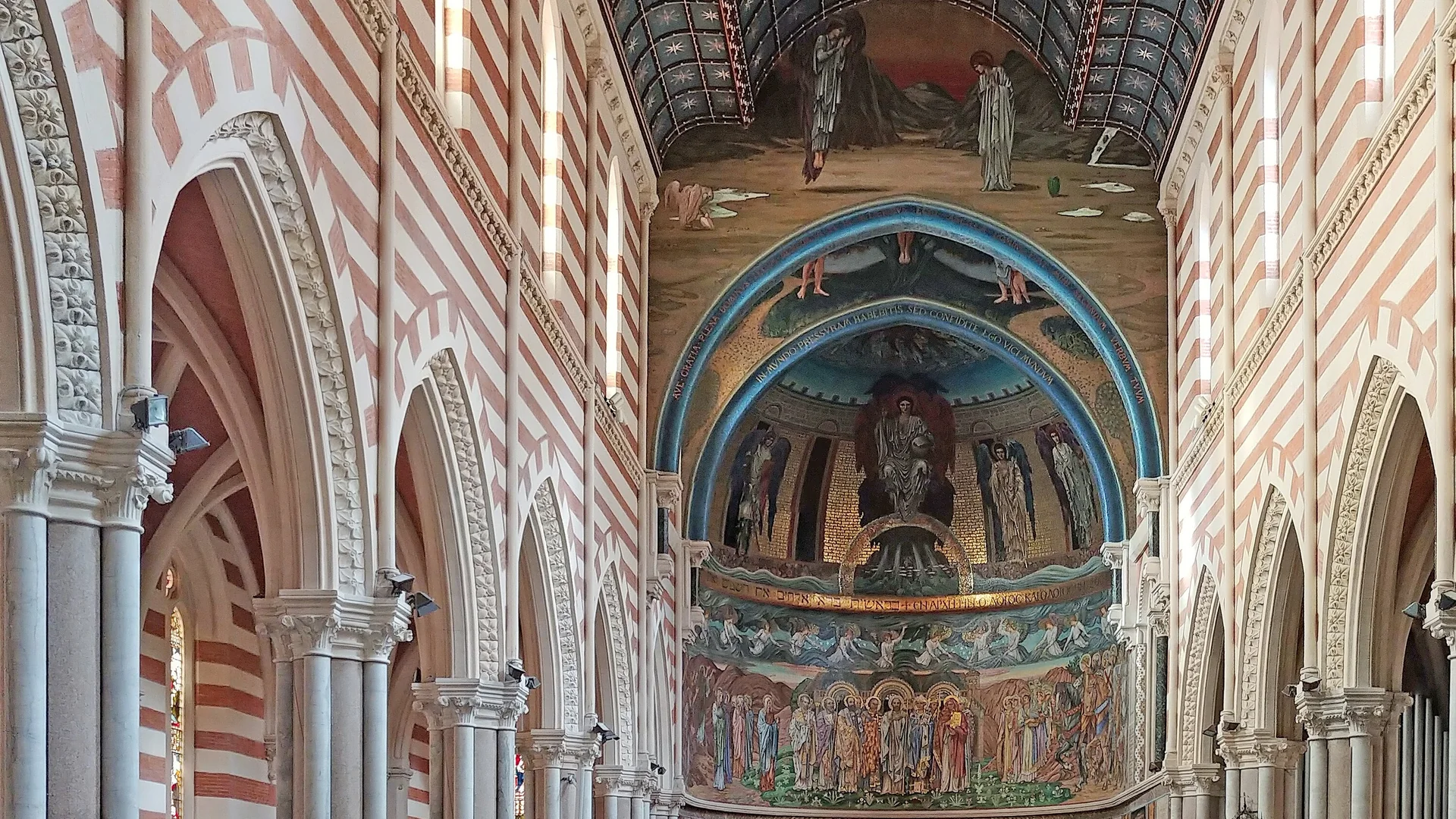 The nave of St Paul's Within the Walls in Rome, with striped red-and-white walls and pointed arches leading to a chancel arch and an apse covered in blue, gold and green mosaics.
